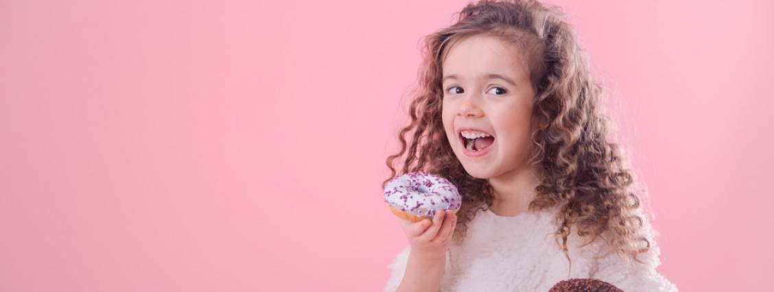 Ein kleines, lockiges Mädchen isst Donuts 